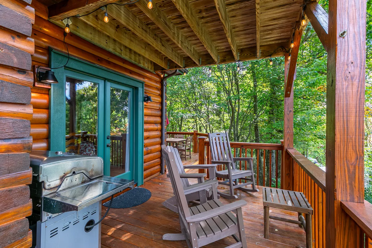 A spacious wooden deck features a grill, rocking chairs, and views of green trees, creating an inviting setting for group barbecues or quiet morning coffees. The deck’s ambiance encourages both lively gatherings and peaceful nature appreciation.