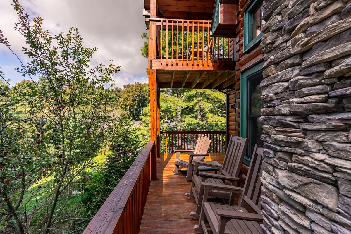 A tranquil wooden deck bordered by greenery, with Adirondack chairs positioned for comfort. The stone wall and surrounding foliage create a cozy nook for wildlife watching or unwinding under the stars.