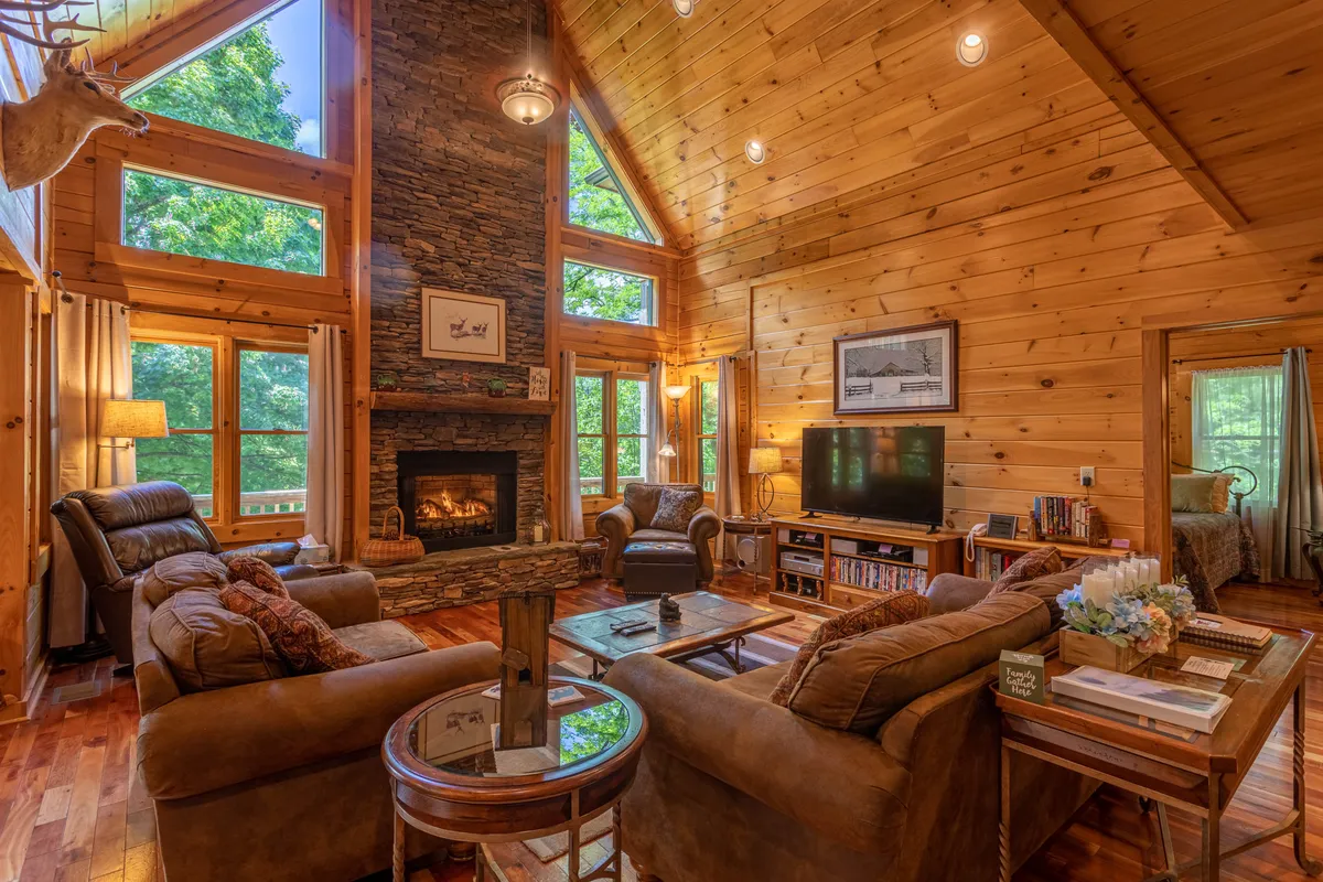 A warm, comfortable living room with large windows framing views of the outdoors, a stone fireplace, and plenty of plush seating. The space feels welcoming and perfectly suited for relaxing while keeping an eye on outside activities through the windows.