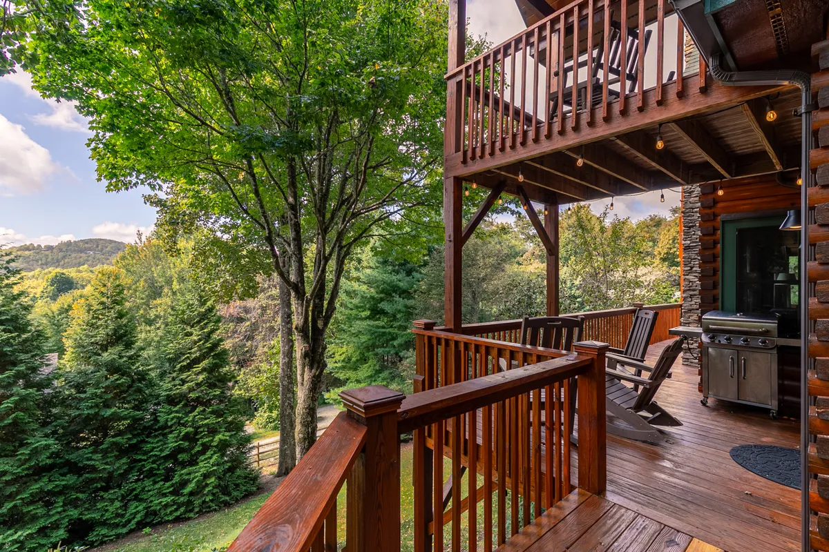A wooden deck overlooking treetops and mountains, equipped with a grill and rocking chairs—ideal for barbecues, outdoor relaxation, and appreciating the natural surroundings.