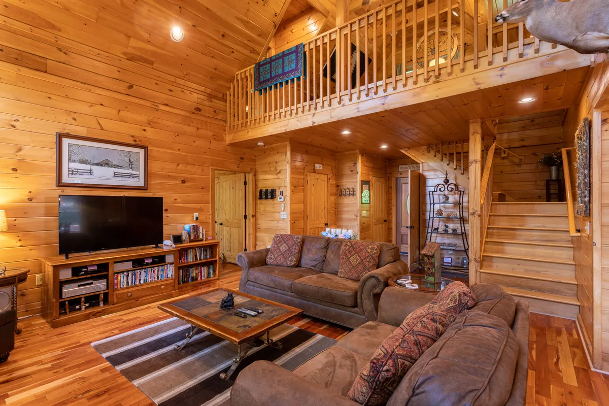 A spacious family room with wooden beams, two large sofas, a coffee table adorned with decorative items, and a large television. The setting is warm and welcoming, perfect for movie nights or group gatherings after a day of adventure.
