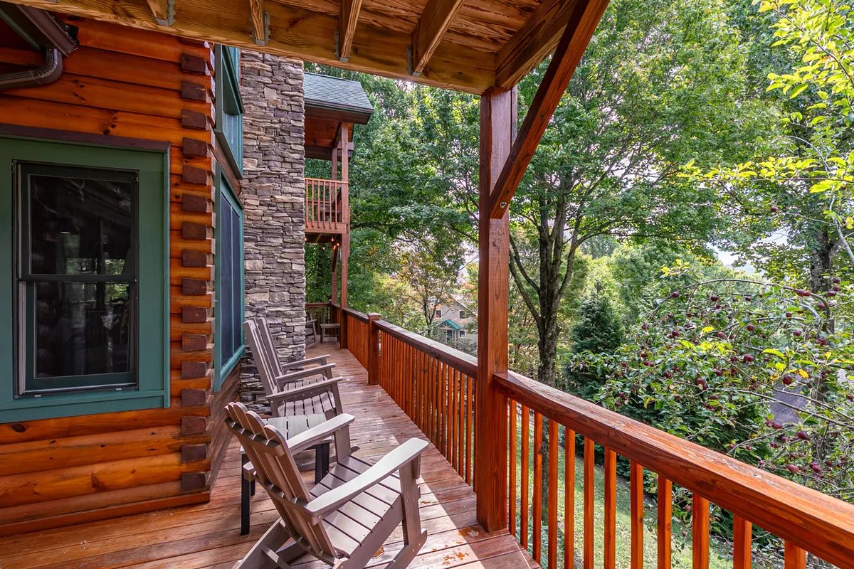 A wooden deck with Adirondack chairs overlooks lush greenery, paired with a stone facade of the cabin. The tranquil atmosphere is perfect for reading, relaxing, or watching pets play safely outdoors.
