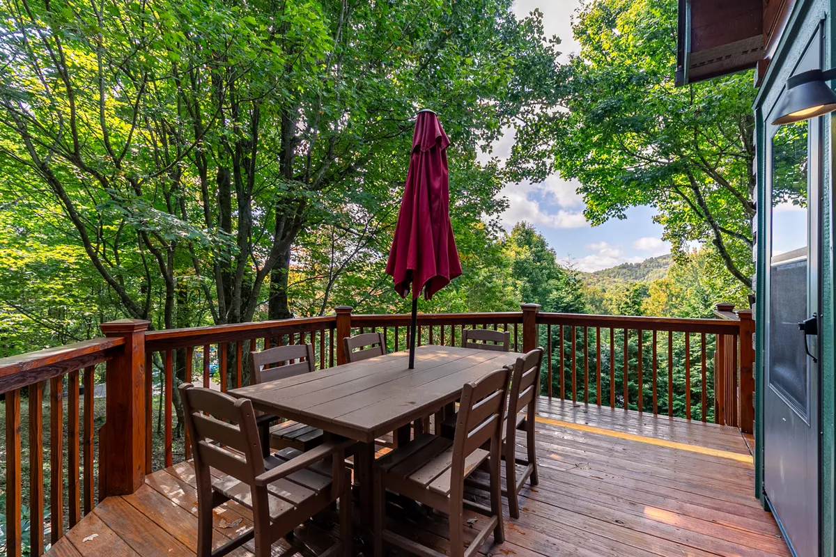 This exterior image features a wooden table with a red umbrella set amidst lush trees, creating a tranquil spot for outdoor dining or relaxing in nature. The surrounding foliage and open-air setting emphasize the connection to the outdoors and the peaceful atmosphere of the property.