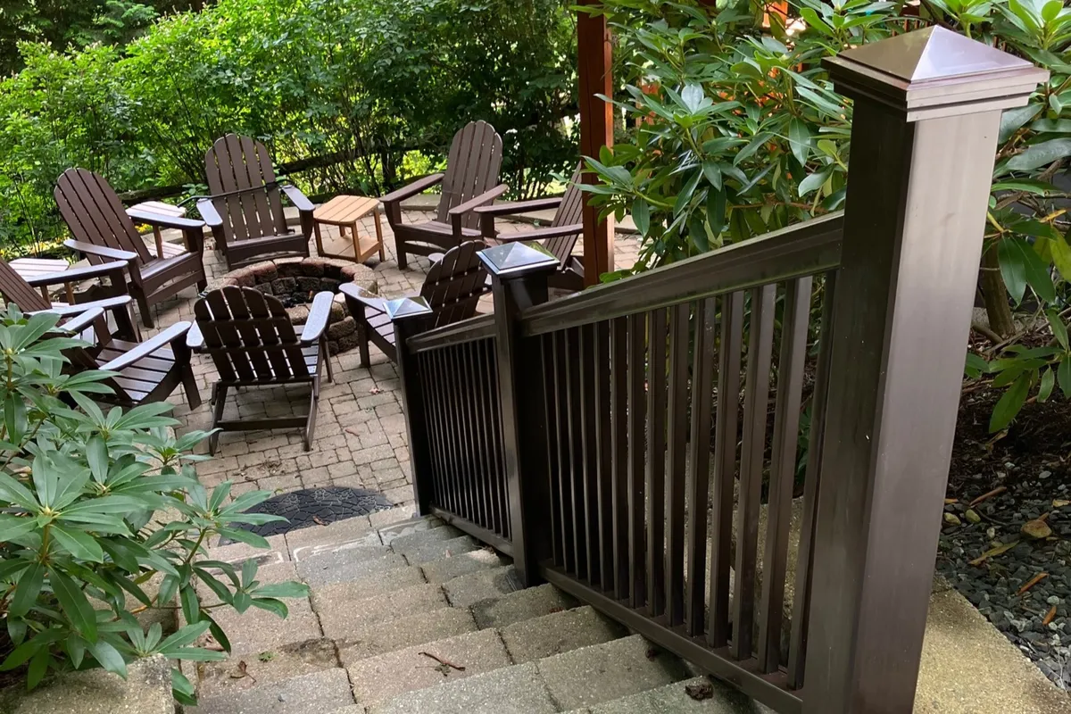 A beautifully landscaped outdoor area featuring an inviting fire pit surrounded by Adirondack chairs and a wooden table, set against a backdrop of lush greenery. The setup is perfect for families to gather in the evening, share stories, and enjoy s'mores under the stars.