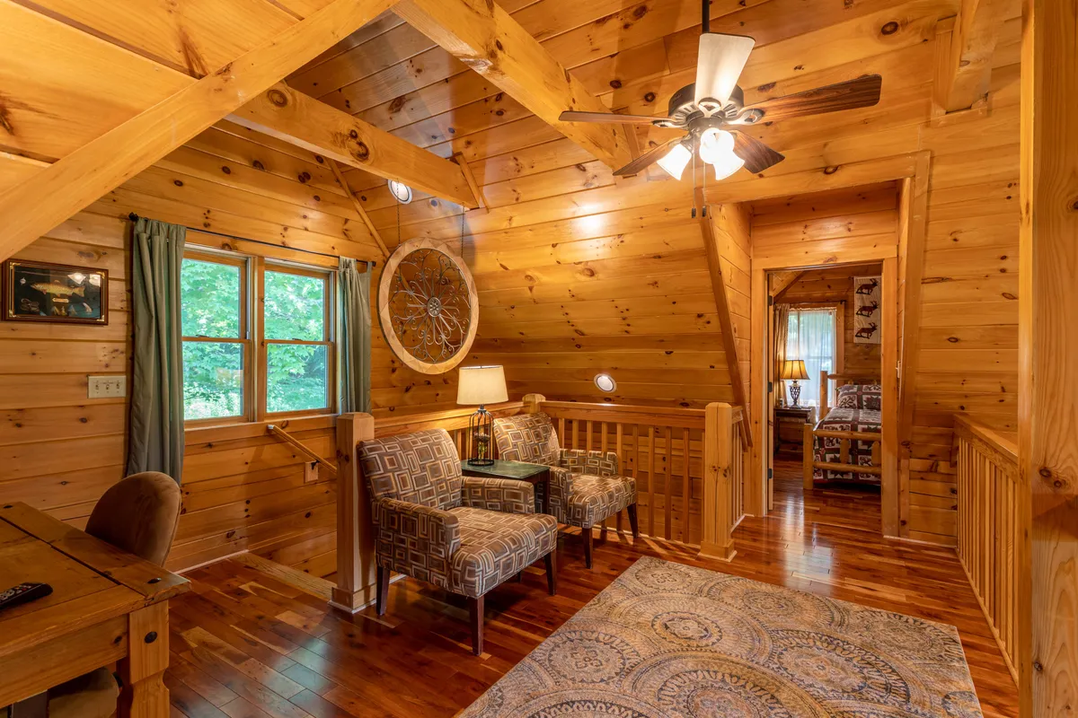 A cozy interior nook with comfortable chairs, a decorative rug, and a window inviting natural light and views of the trees outside. The setup encourages reading, relaxing, or enjoying the natural scenery, blending indoor comfort with a connection to the outdoors.