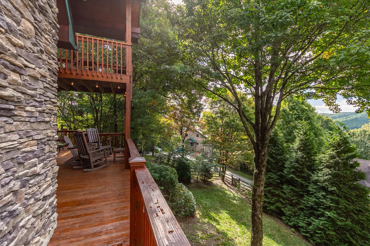 A serene exterior deck scene with classic wooden rocking chairs facing a lush mountain backdrop. The deck is bordered by a stone wall and surrounded by greenery, inviting guests to relax with coffee at sunrise or drinks at sunset.